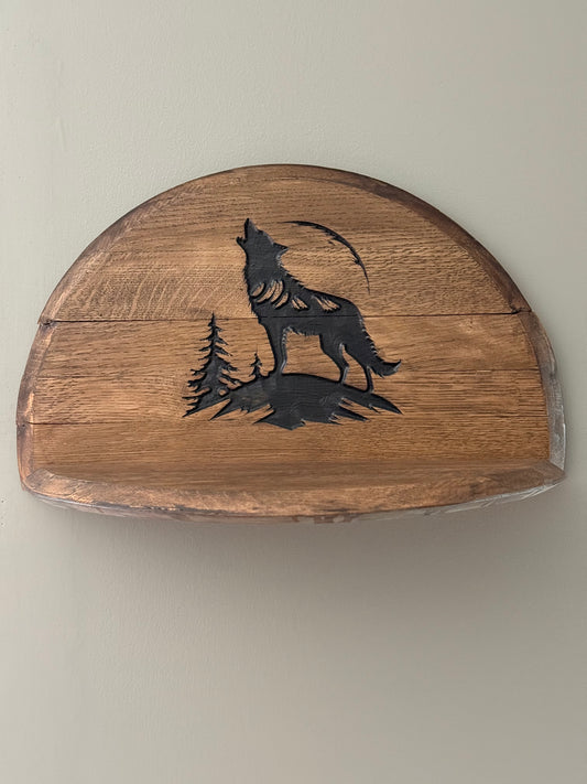 Bourbon barrel lids split to create a shelf . Lid engraved with image of wolf howling on mountaintop and two pine trees in background.