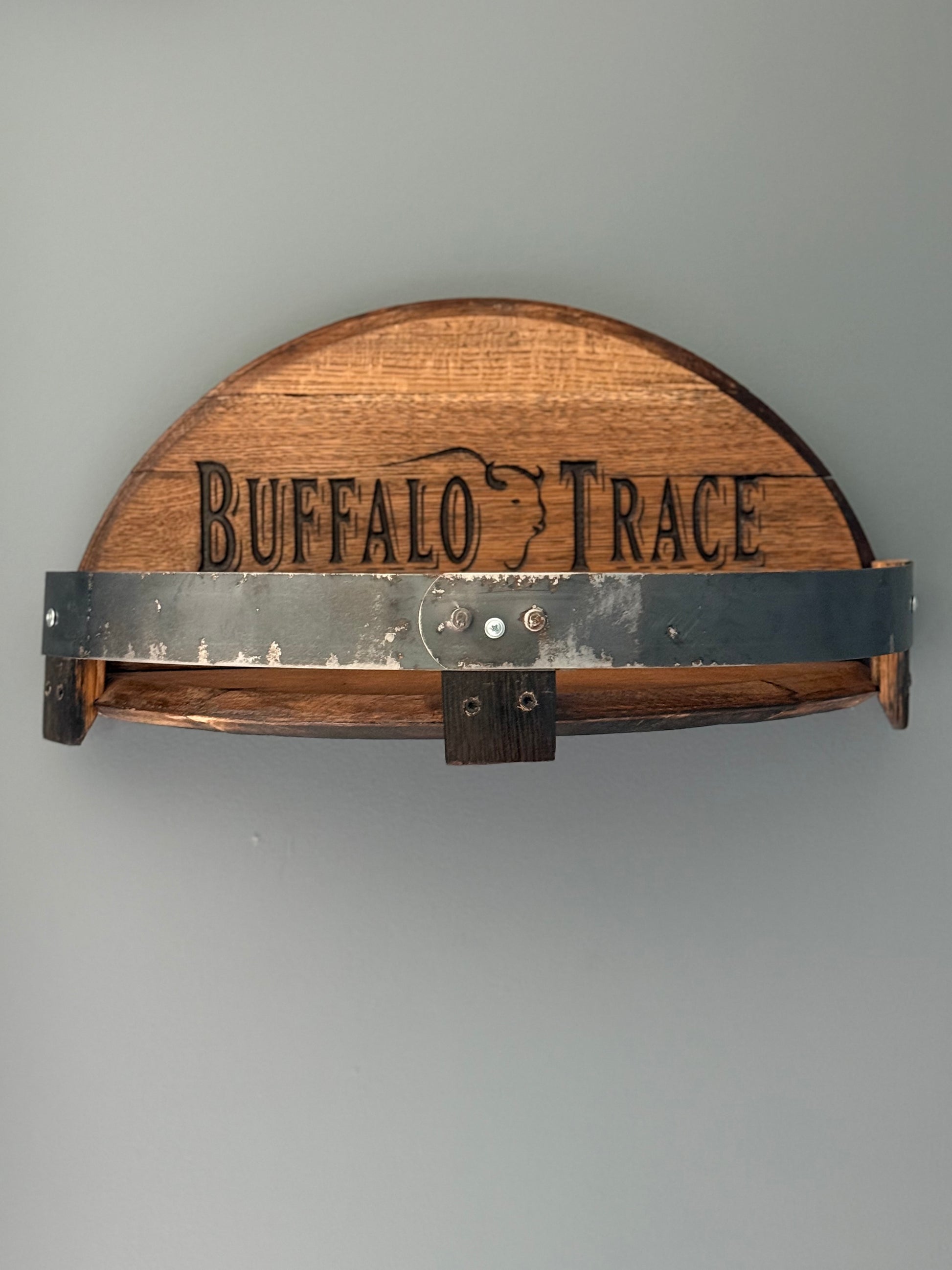 Bourbon barrel lids split to create a shelf bordered by small pieces of stave with metal barrel band. Lid engraved with "Buffalo Trace" and outline of buffalo in center.