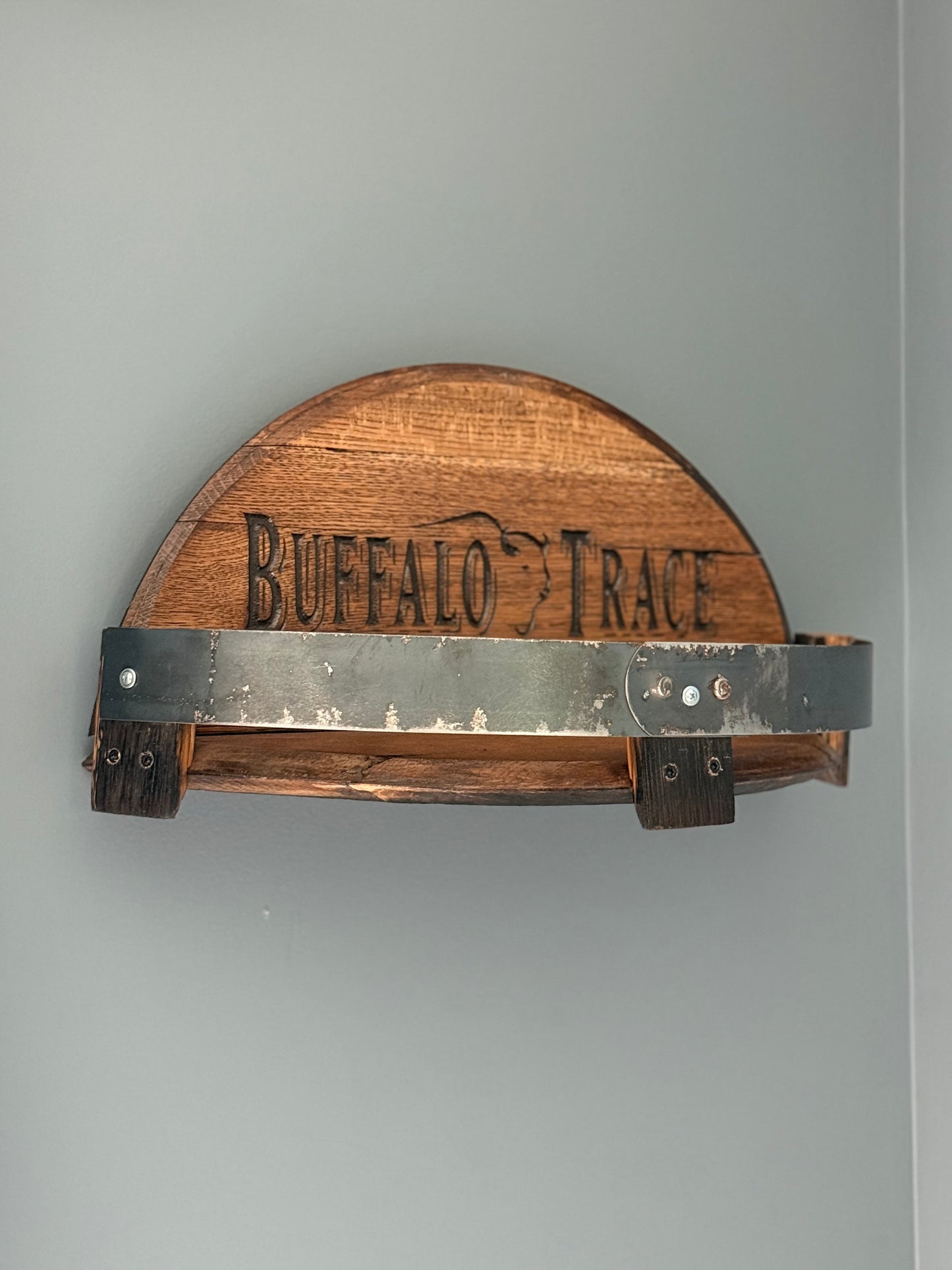 Bourbon barrel lids split to create a shelf bordered by small pieces of stave with metal barrel band. Lid engraved with "Buffalo Trace" and outline of buffalo in center.