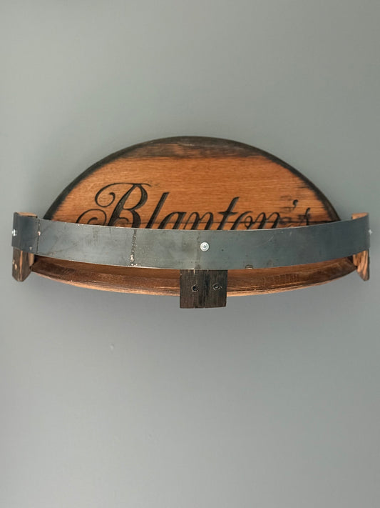 Bourbon barrel lids split to create a shelf bordered by small pieces of stave with metal barrel band. Lid engraved with "Blanton's".